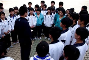 操场上一群穿校服的学生围成一圈,中间的社工正在讲话